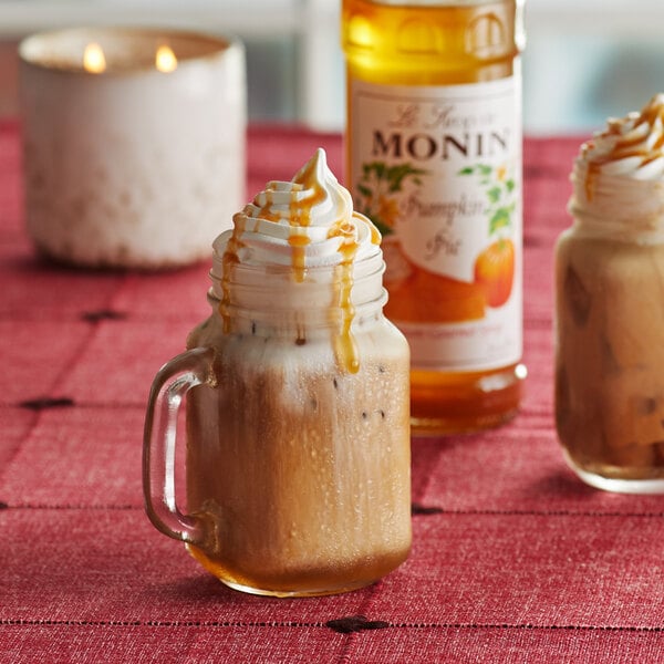 A glass mug of iced coffee with whipped cream and Monin Pumpkin Pie Syrup.