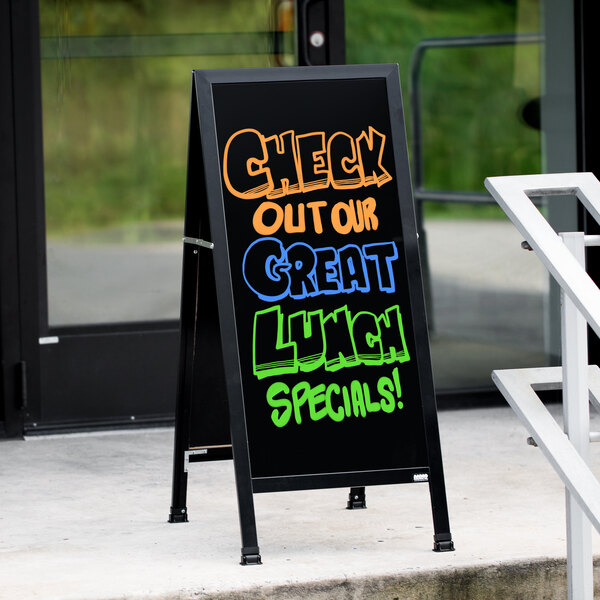 An Aarco black aluminum A-frame sign with a black marker board that says "Check out our great lunch specials" on a sidewalk.