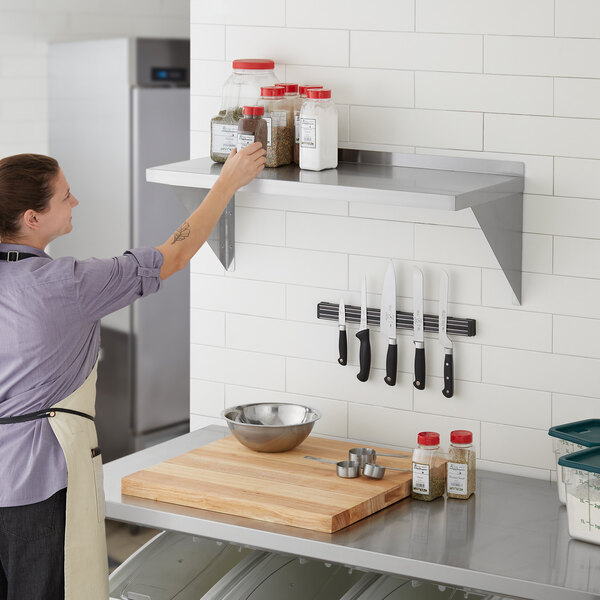 A woman holding a Regency stainless steel wall shelf in a professional kitchen.