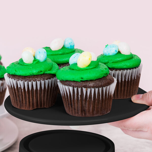 A hand holding a black tray of cupcakes with green frosting and candy eggs on top.