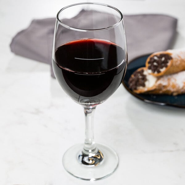 A Libbey wine goblet filled with red wine on a table with pastries.