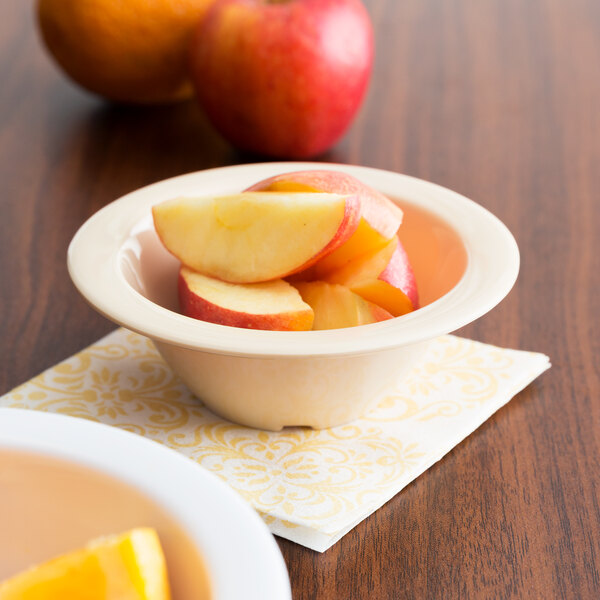 A bowl of fruit including sliced apples and oranges on a table.