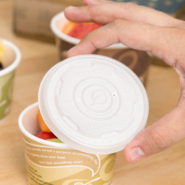 A hand holding a white Eco-Products plastic lid on a small container of fruit.