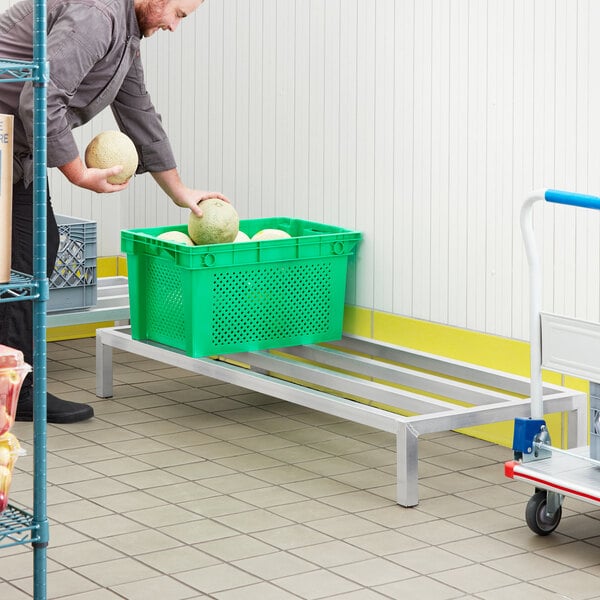 A man using a green cart to move a Regency aluminum dunnage rack.