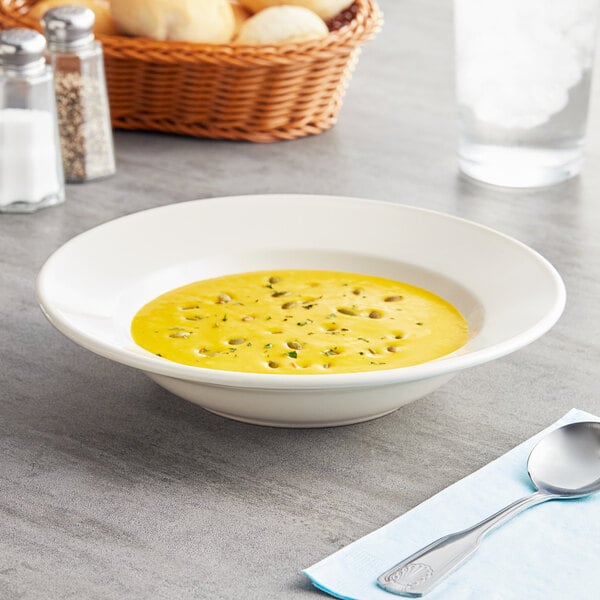 An Acopa ivory stoneware soup bowl on a table with a spoon and bread.