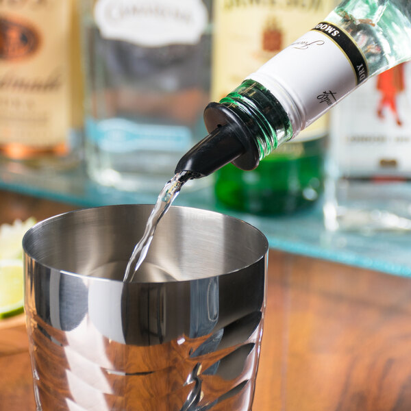 A Tablecraft black liquor pourer on a bottle pouring liquid into a metal cup.