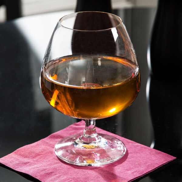 A Spiegelau Soiree Cognac glass of brown liquid on a pink cloth.