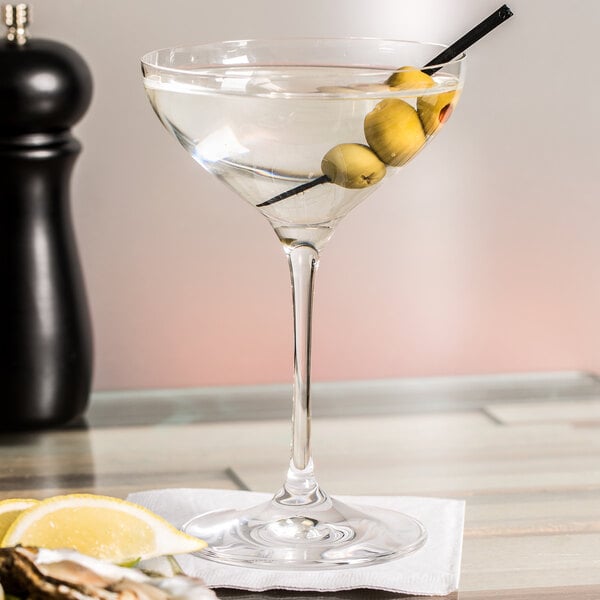 A Spiegelau cocktail glass with olives and a lemon wedge in it.