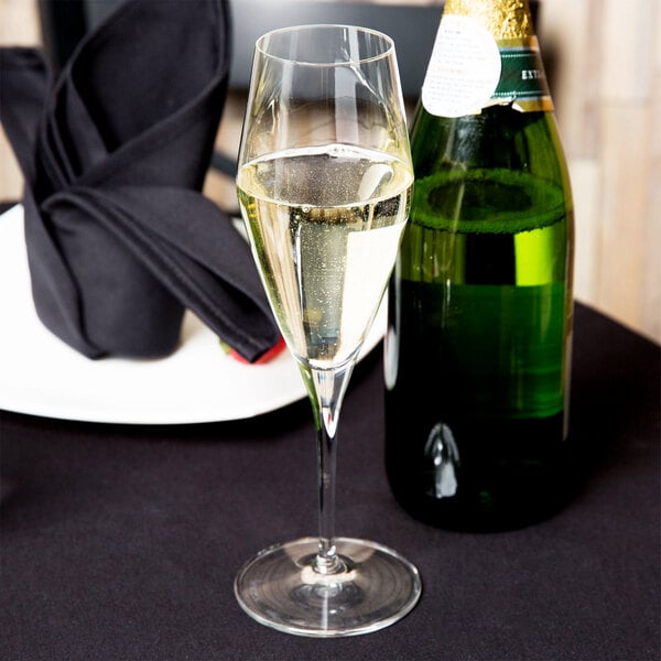 A Spiegelau flute filled with champagne sits on a table next to a bottle of champagne.