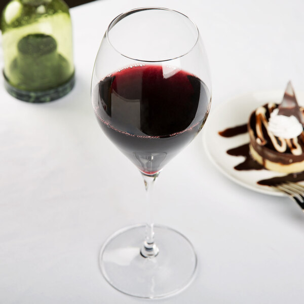 A close-up of a Spiegelau Adina Prestige Bordeaux wine glass filled with red wine on a table.