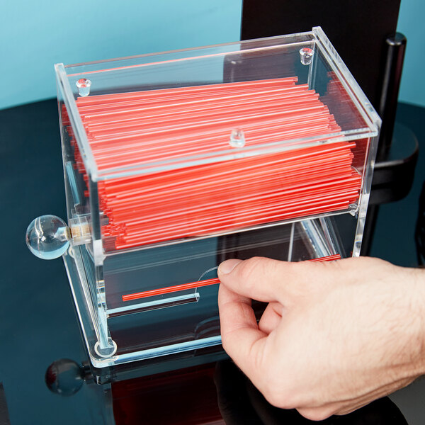 A hand holding a plastic box with red stir sticks in a Cal-Mil straw organizer.