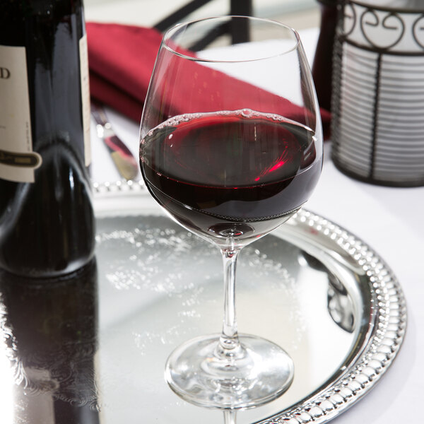 A Spiegelau Vino Grande burgundy wine glass filled with red wine on a silver tray.