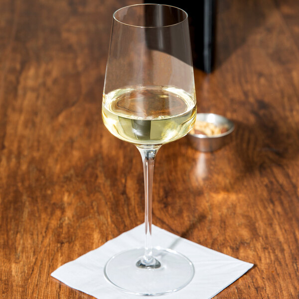 A Spiegelau white wine glass filled with white wine on a table.
