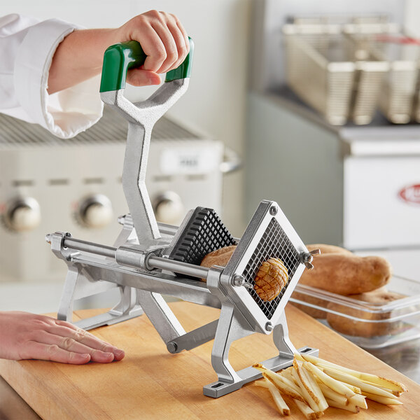 A hand using a Garde heavy-duty French fry cutter with a green handle to cut a potato.