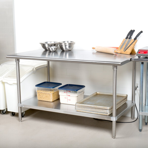 An Advance Tabco stainless steel work table with a metal shelf holding food containers.
