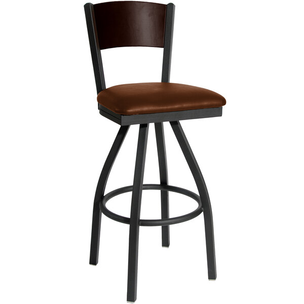 A BFM Seating black metal swivel restaurant bar stool with a walnut finish wooden back and light brown vinyl seat.