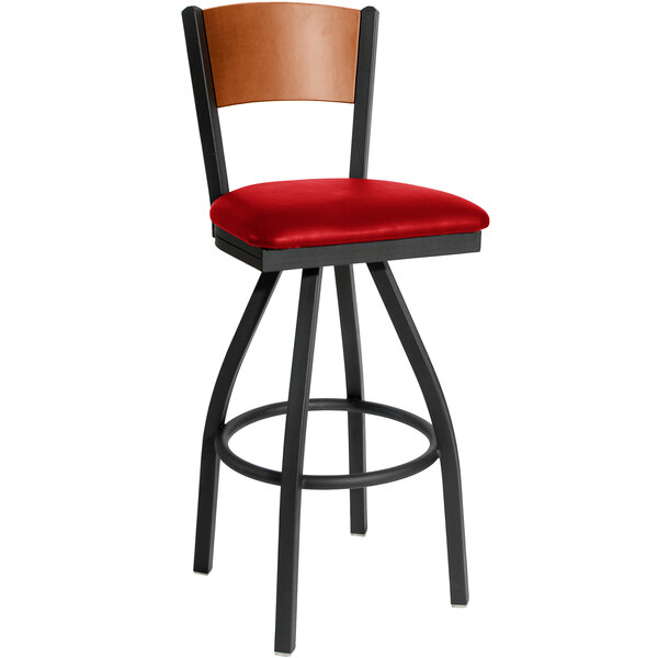 A black metal BFM Seating swivel restaurant bar stool with cherry finish wooden back and red vinyl seat.