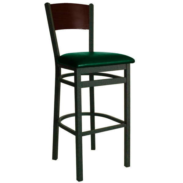 A BFM Seating black metal bar stool with a walnut back and green vinyl seat.