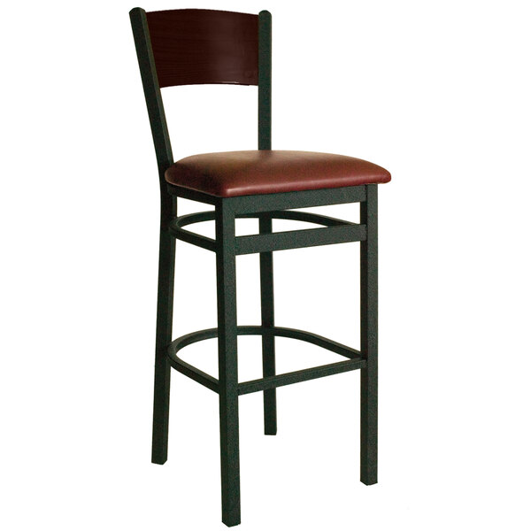 A BFM Seating black metal bar stool with a walnut finish wooden back and burgundy vinyl seat.