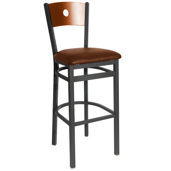 A BFM Seating black metal bar stool with a light brown vinyl seat and cherry wooden back.