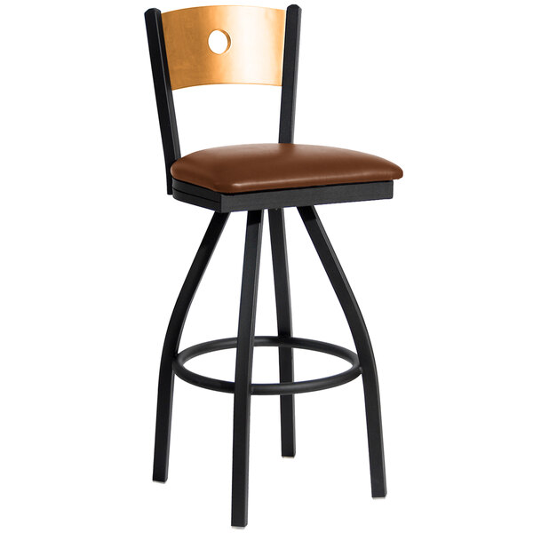 A BFM Seating black metal bar stool with a natural wood back and light brown vinyl swivel seat.