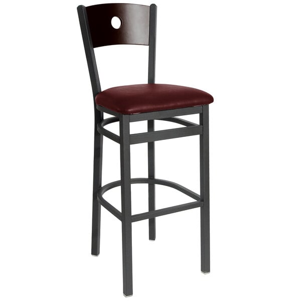 A BFM Seating black metal bar stool with a walnut wooden back and burgundy vinyl seat.