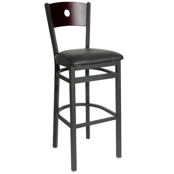 A BFM Seating black metal bar chair with black vinyl seat and mahogany wood back.