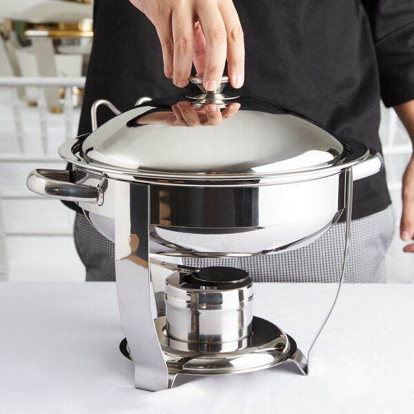 A person holding a Vollrath stainless steel Orion lift-off chafing dish over a table.