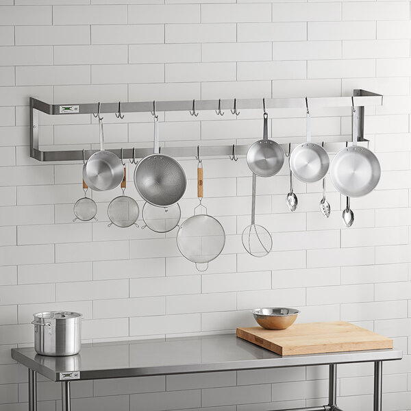 A kitchen with Regency stainless steel pot racks holding pots and pans on a wall.