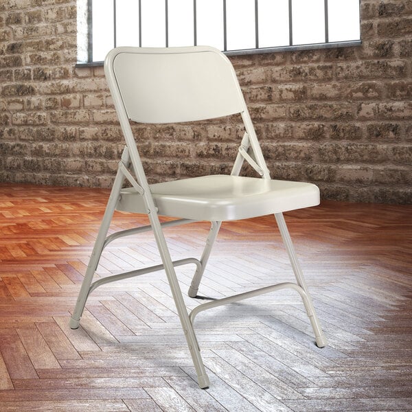 A gray National Public Seating folding chair in front of a brick wall.