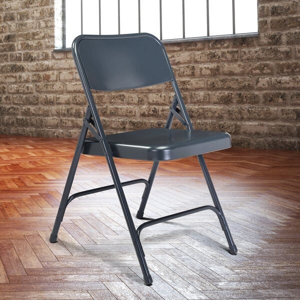 A National Public Seating metal folding chair in front of a brick wall.