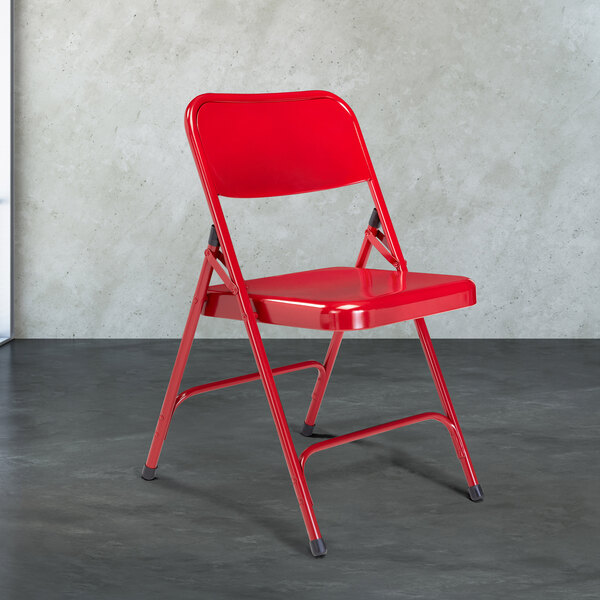 A red National Public Seating metal folding chair on a gray surface.