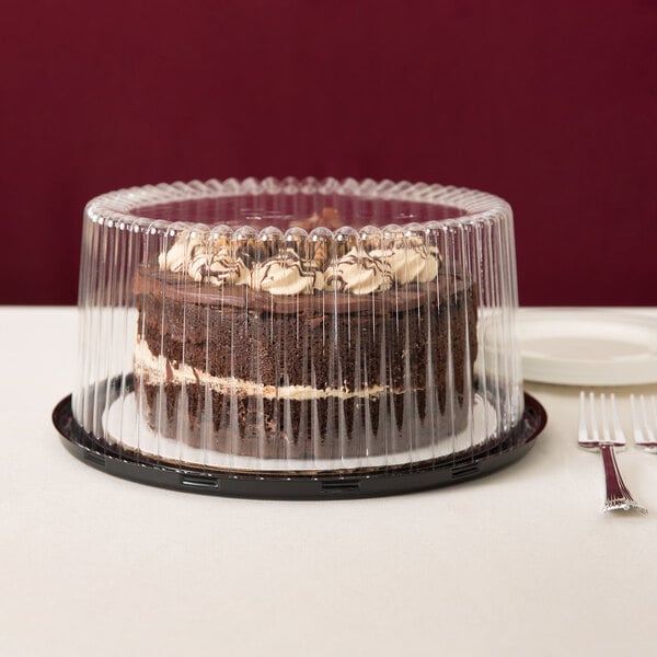 A chocolate cake in a D&W Fine Pack plastic container with a clear lid on a table in a bakery display.