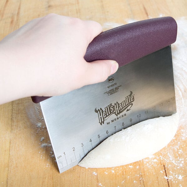 A person using a Mercer Culinary stainless steel dough cutter to cut dough.