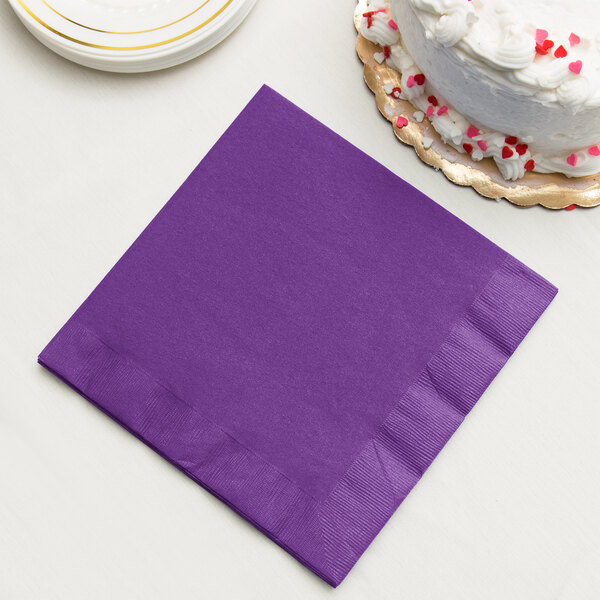 A Creative Converting amethyst purple paper dinner napkin next to a white cake.