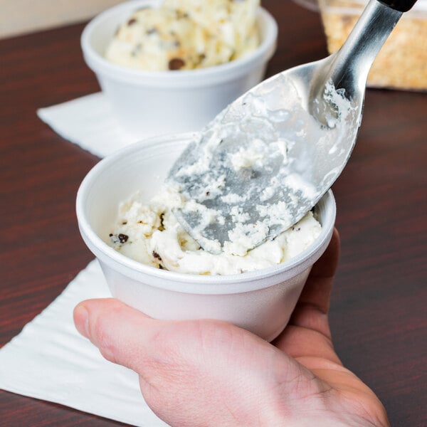 A person using a Tablecraft stainless steel ice cream spade to scoop ice cream into a bowl.