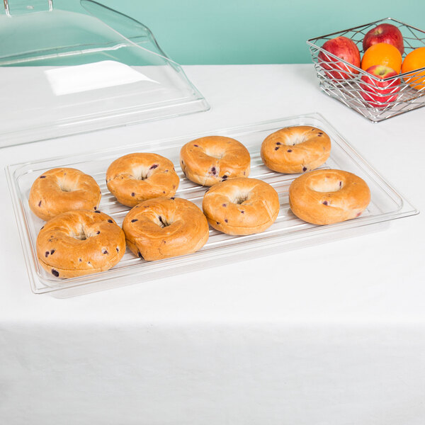 A Cambro clear market tray with bagels and a bagel with blueberries on it on a table with a bowl of fruit.