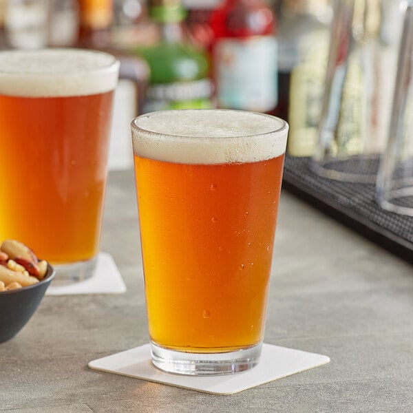 Two Acopa mixing glasses filled with beer on a bar table with a bowl of peanuts.