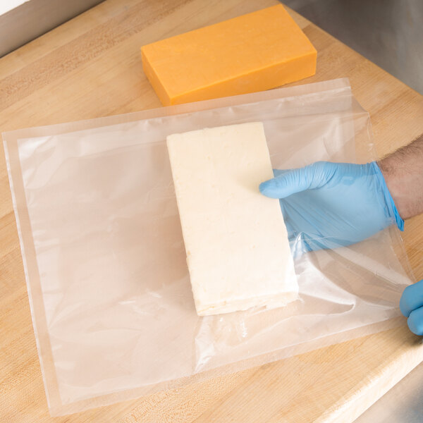A person in blue gloves using an ARY VacMaster gallon-size plastic bag to vacuum seal a block of cheese.
