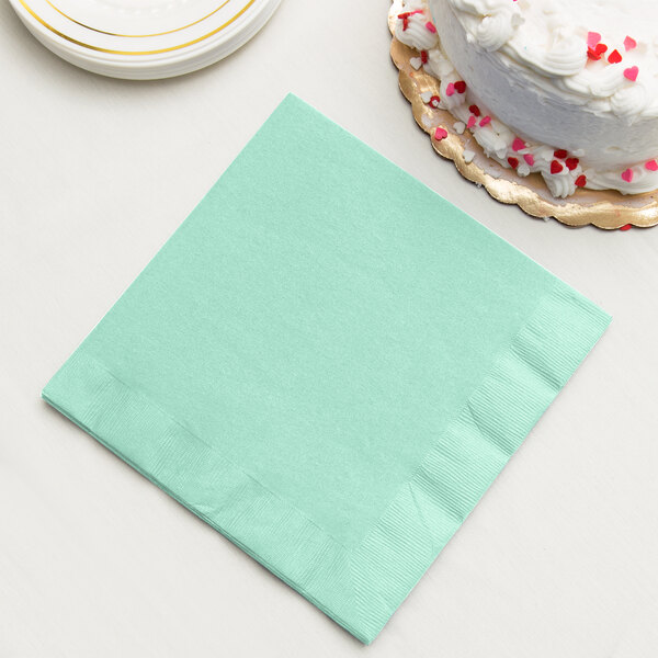 A Fresh Mint Green Creative Converting paper napkin next to a white cake.