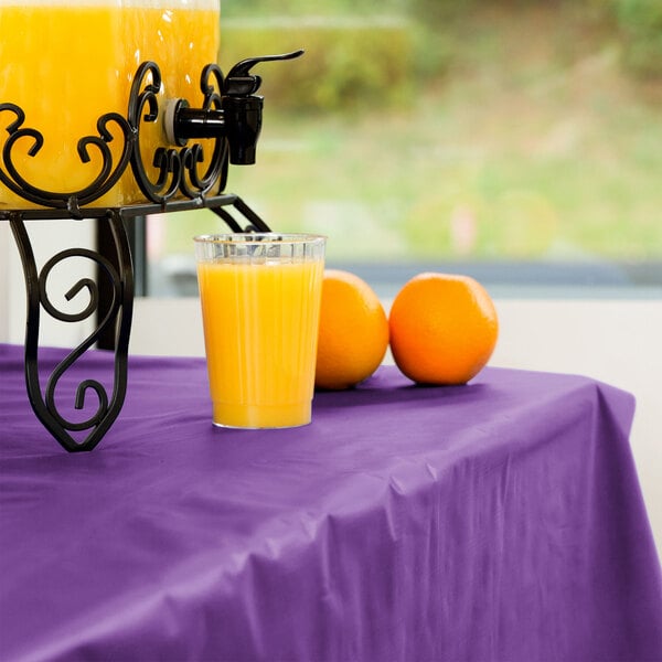 A glass of orange juice on an amethyst purple table with oranges.
