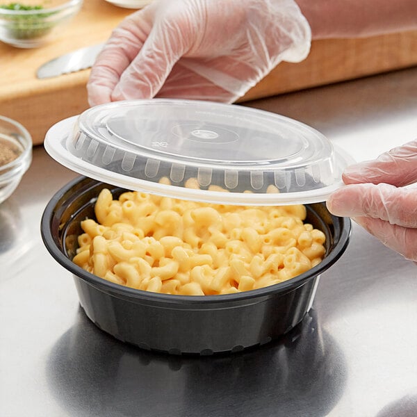 A person using a Choice black plastic microwaveable container and lid to store macaroni and cheese.