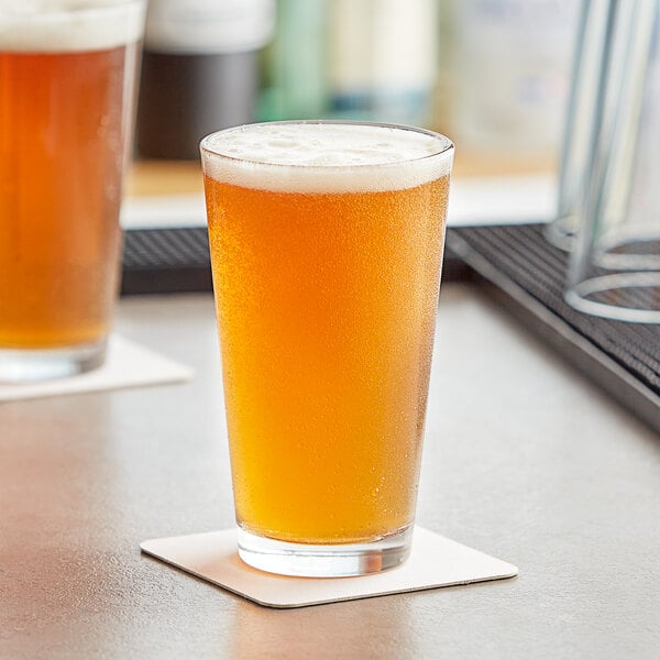 Two Acopa Select customizable pint glasses of beer on a table with foam on one glass.