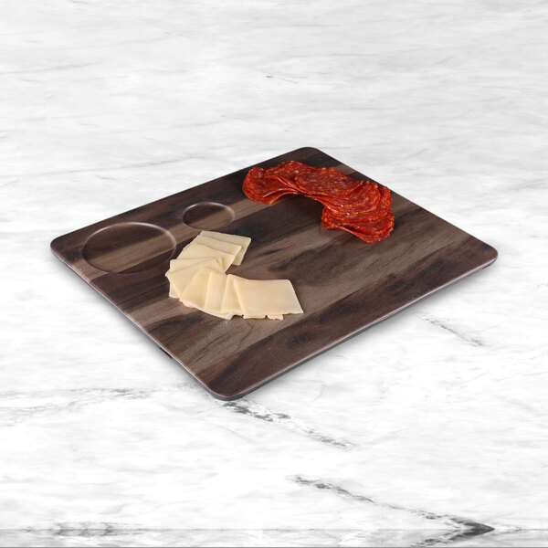An Elite Global Solutions faux hickory serving board with double ramekin compartments holding slices of meat and cheese on a counter.