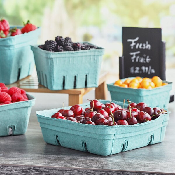 A group of green molded pulp produce baskets filled with berries on a table.