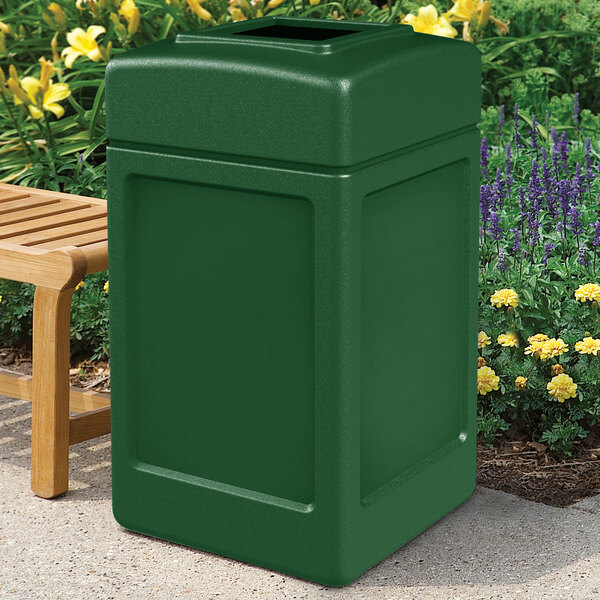A forest green Commercial Zone PolyTec waste container next to a bench.