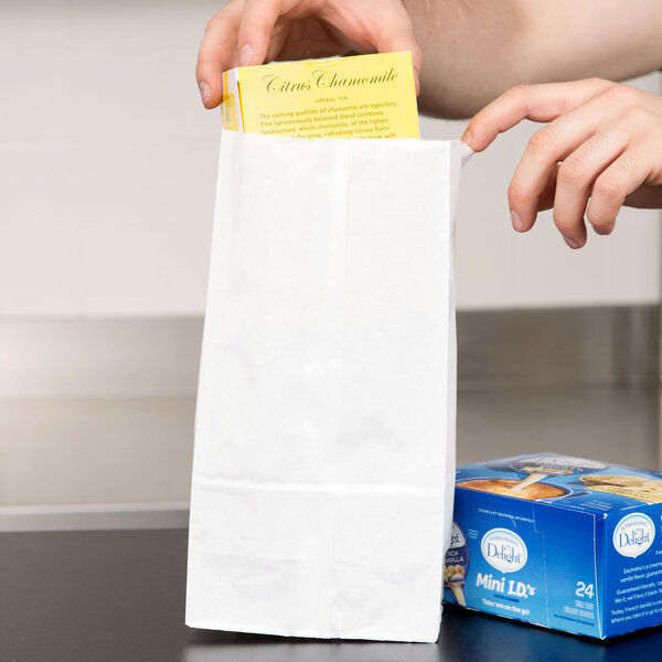 A person holding a white paper bag of tea over a box with a blue label.