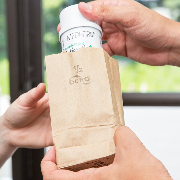 A person's hands holding a Duro brown paper bag with a medicine bottle inside.