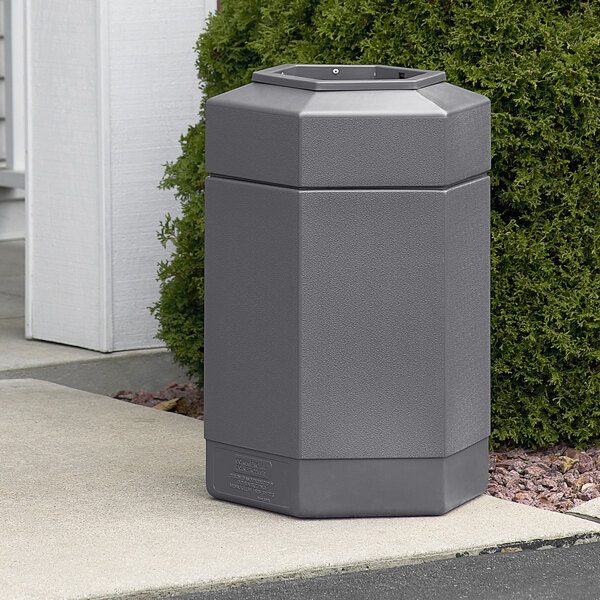 A Commercial Zone gray hexagonal waste container sitting on a sidewalk.