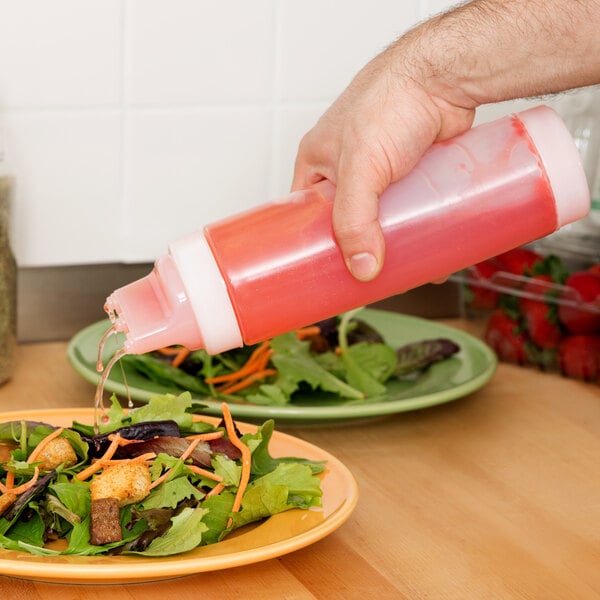 A hand using a Tablecraft SelecTop squeeze bottle to pour pink liquid onto a salad.
